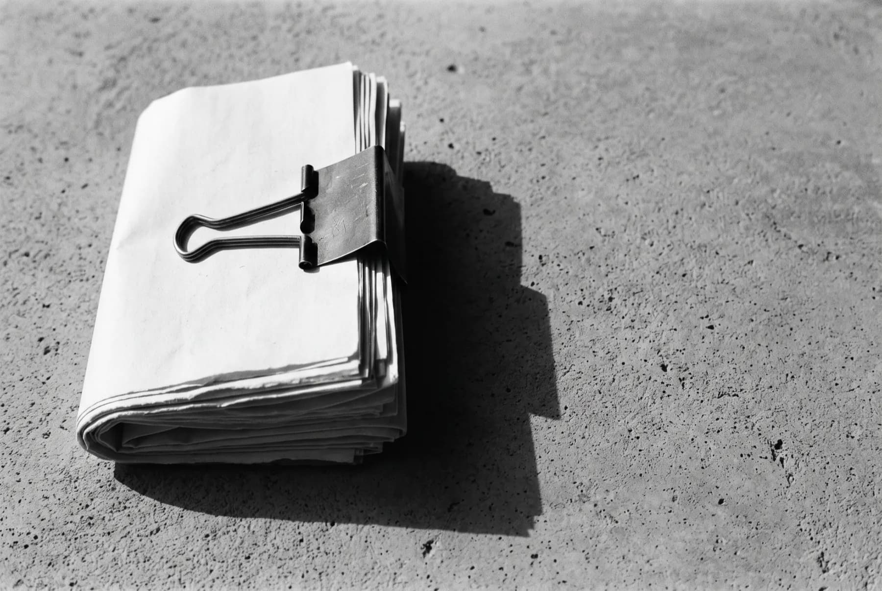 A clipped stack of paper documents resting on raw concrete